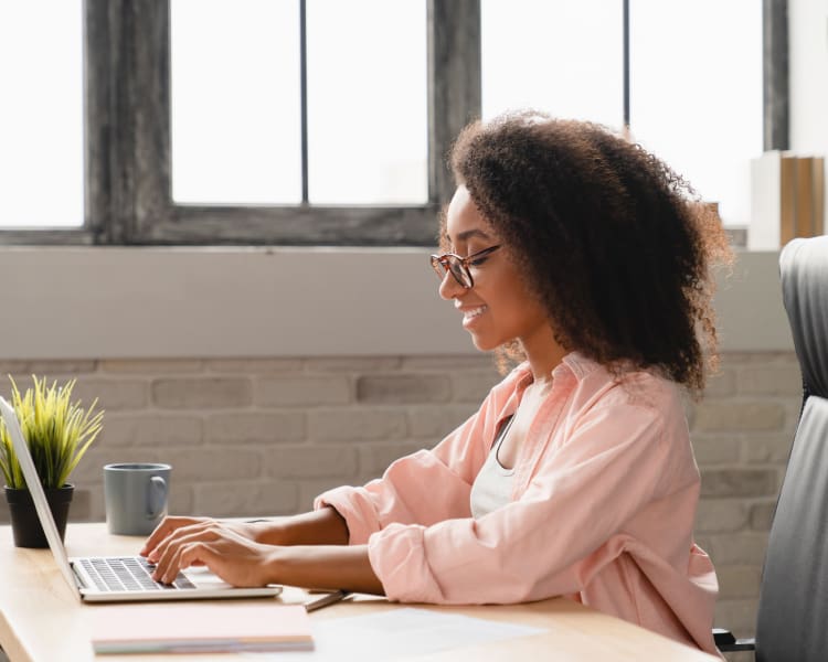 Seo-Fundamentals-Keywords-Marketing A woman focused on her laptop, seated at her office desk, surrounded by books and office supplies, engaged in her work.