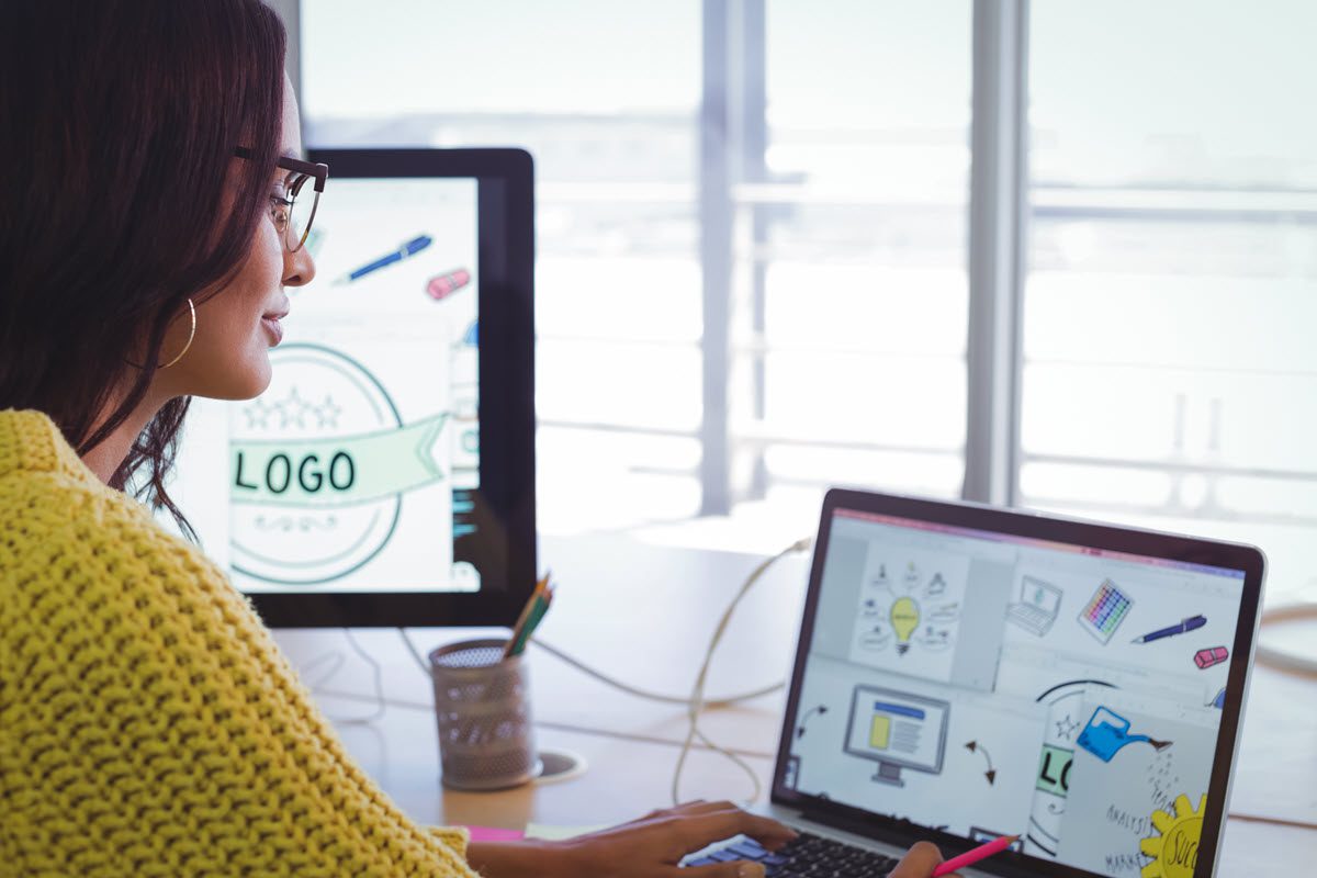 A woman working on a laptop displaying a logo, focused on web design and custom logo development tasks.